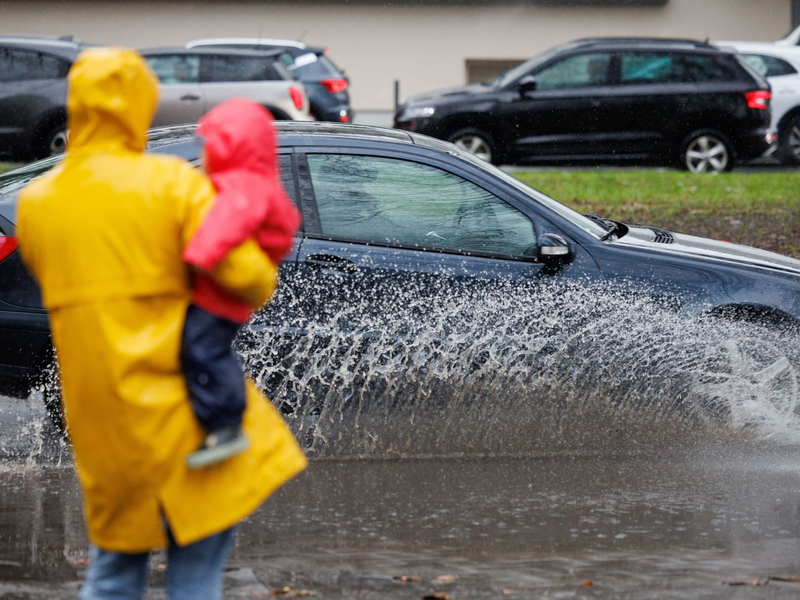 Eine Mutter und ihr Kind blicken auf eine teils überflutete Straße in Osnabrück. - Foto: Friso Gentsch/dpa