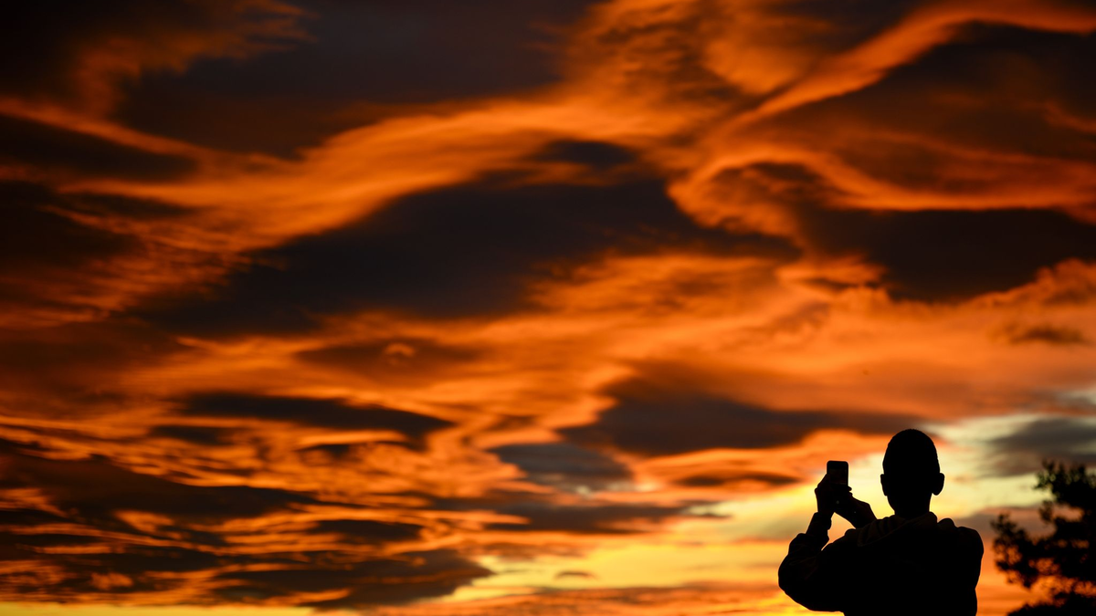 Das Naturschauspiel festhalten: Ein Mann fotografiert einen Sonnenuntergang. - Foto: Laurent Gillieron/KEYSTONE/dpa