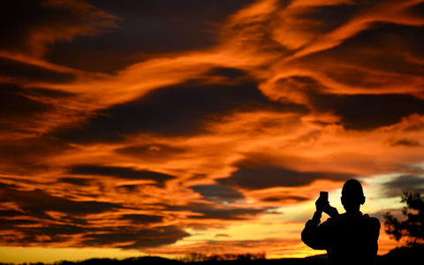 Das Naturschauspiel festhalten: Ein Mann fotografiert einen Sonnenuntergang. - Foto: Laurent Gillieron/KEYSTONE/dpa