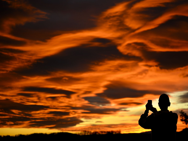 Das Naturschauspiel festhalten: Ein Mann fotografiert einen Sonnenuntergang. - Foto: Laurent Gillieron/KEYSTONE/dpa