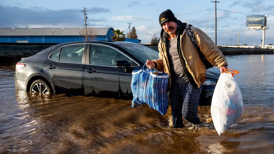 Ein Mann trägt im Januar in Merced, Kalifornien, Habseligkeiten aus seinem überfluteten Haus. - Bild: Noah Berger/AP/dpa