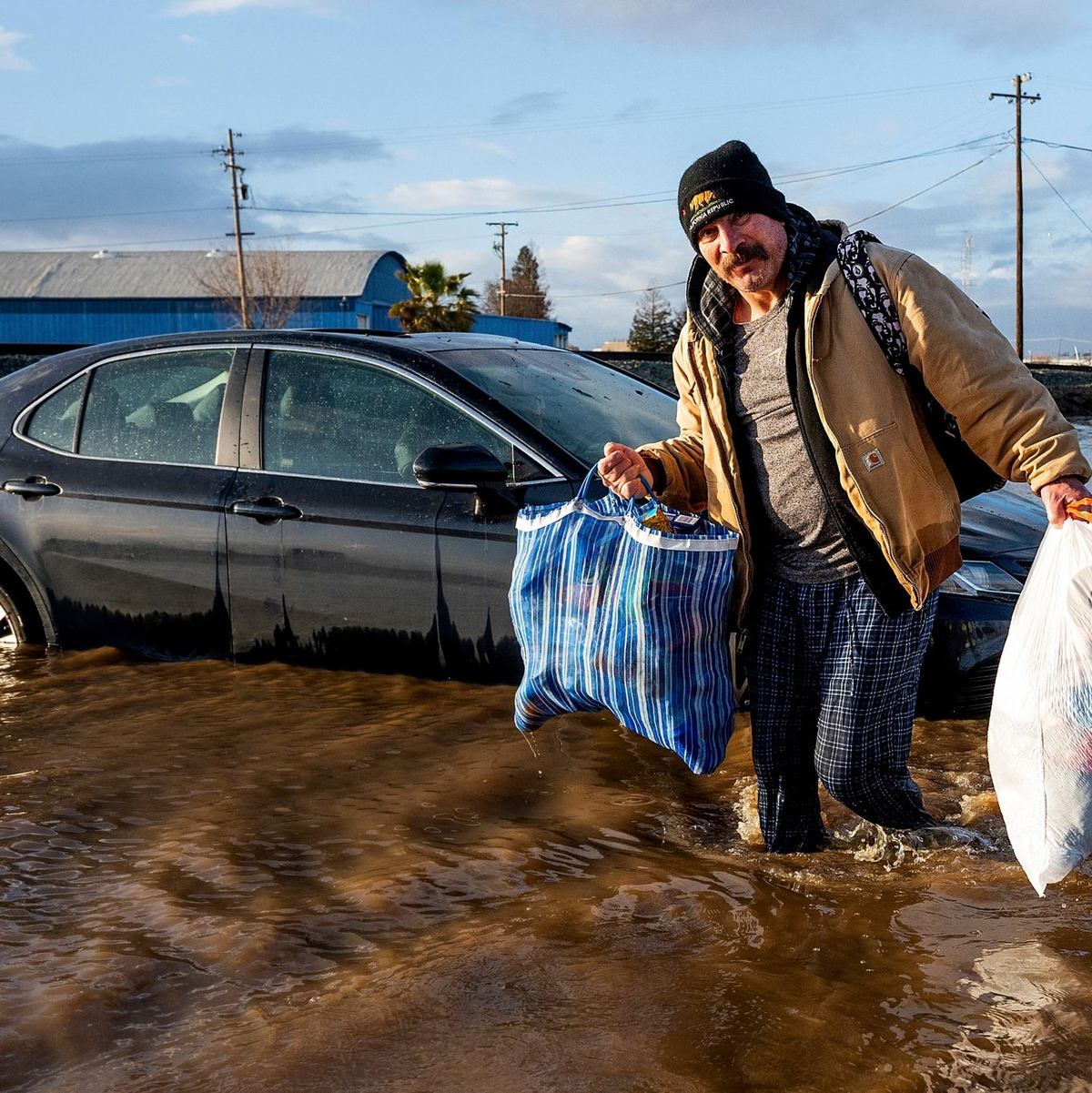 Ein Mann trägt im Januar in Merced, Kalifornien, Habseligkeiten aus seinem überfluteten Haus. - Foto: Noah Berger/AP/dpa