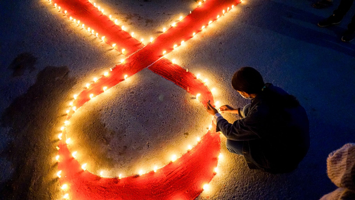 Eine Frau stellt Kerzen auf, die eine rote Schleife formen - ein weltweit anerkanntes Symbol für die Solidarität mit HIV-Infizierten. - Foto: Sunil Pradhan/SOPA Images via ZUMA Wire/dpa