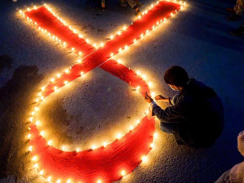 Eine Frau stellt Kerzen auf, die eine rote Schleife formen - ein weltweit anerkanntes Symbol für die Solidarität mit HIV-Infizierten. - Foto: Sunil Pradhan/SOPA Images via ZUMA Wire/dpa