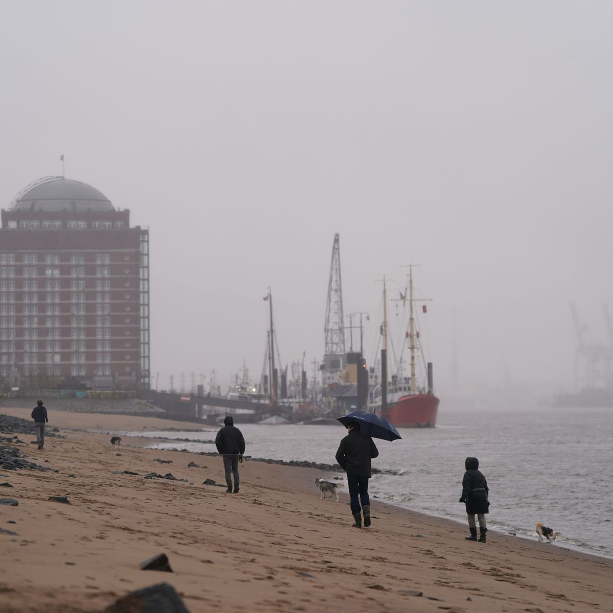 Passanten gehen im strömenden Regen am Elbstrand in Ovelgönne spazieren. - Foto: Marcus Brandt/dpa