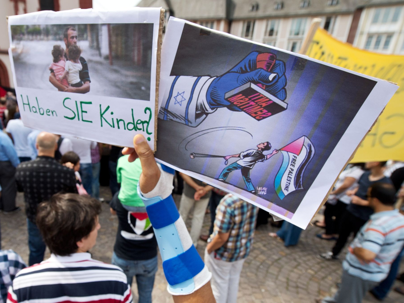 Ein Junge hält ein Plakat hoch, auf dem ein propalästinensischer Demonstrant unter einem Stempel mit der Aufschrift Anti Semitismus steht. - Foto: picture alliance / dpa