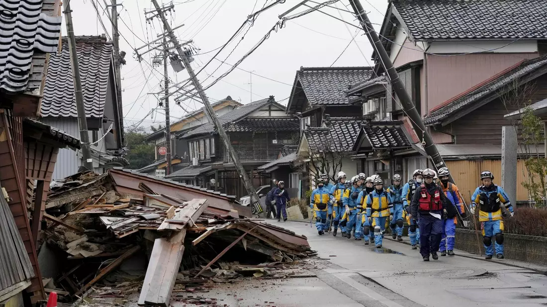 Polizisten gehen an eingestürzten Häusern vorbei, die von den Erdbeben in Suzu, Präfektur Ishikawa getroffen wurden. - Bild: Uncredited/Kyodo News/AP/dpa