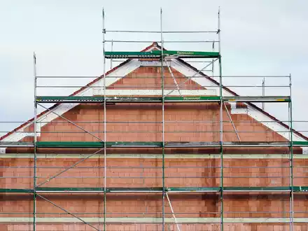 Ein Baugerüst steht in einem Neubaugebiet an einem Rohbau. - Foto: Uwe Anspach/dpa