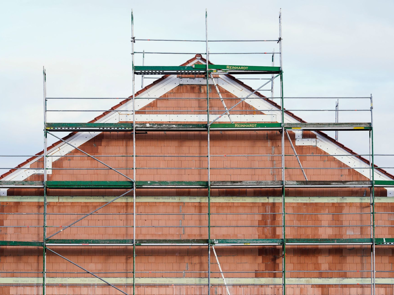 Ein Baugerüst steht in einem Neubaugebiet an einem Rohbau. - Foto: Uwe Anspach/dpa