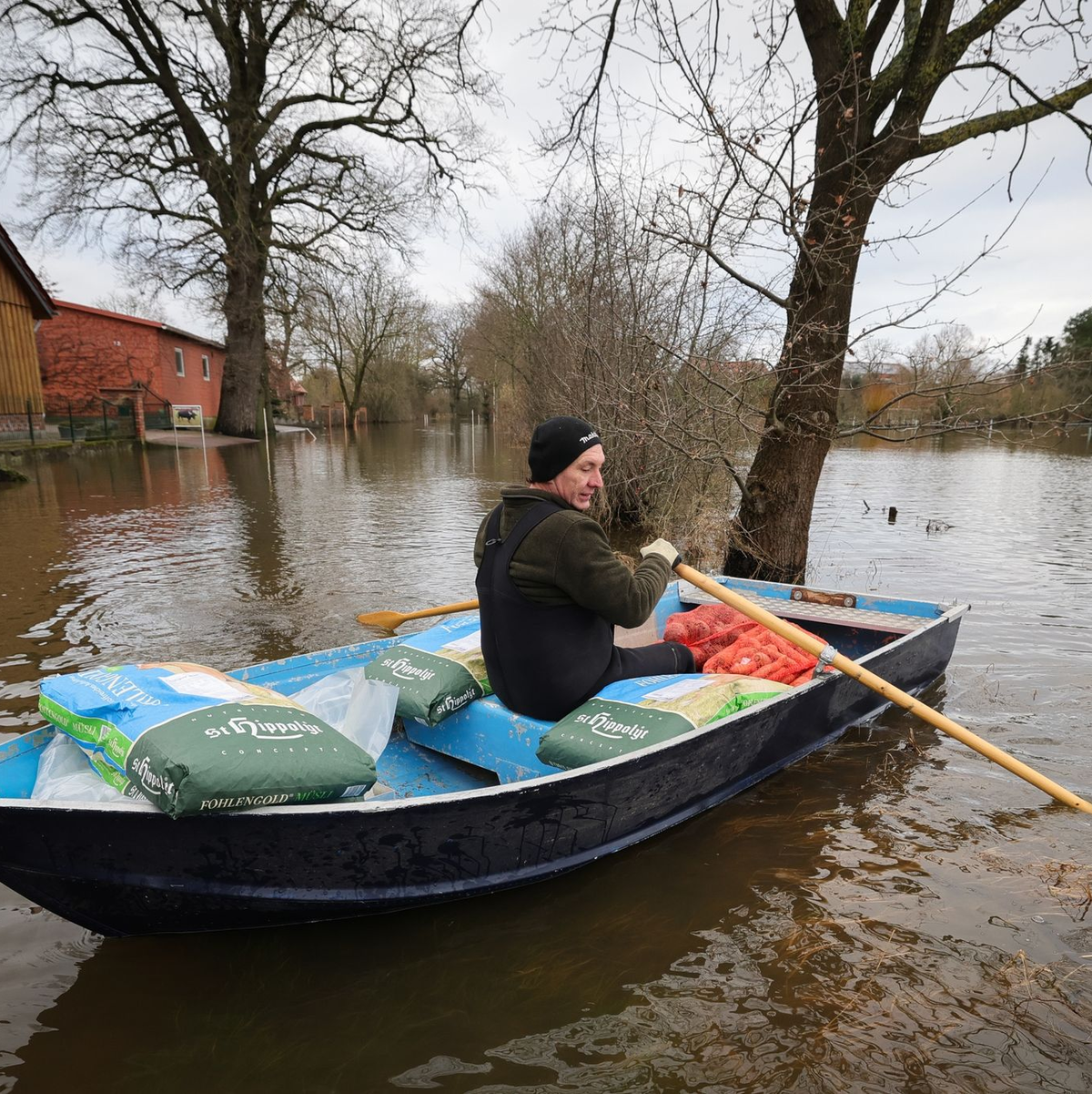 Ein Anwohner bringt mit einem kleinen Ruderboot Futter für seine Tiere über eine überschwemmte Straße in Hagen-Grinden zu seinem Hof. - Foto: Christian Charisius/dpa