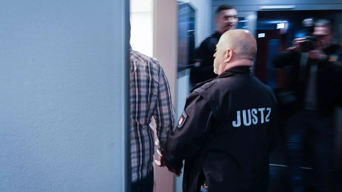 Ein Justizbeamter begleitet den Angeklagten in den Gerichtssaal. - Bild: Rabea Gruber/dpa