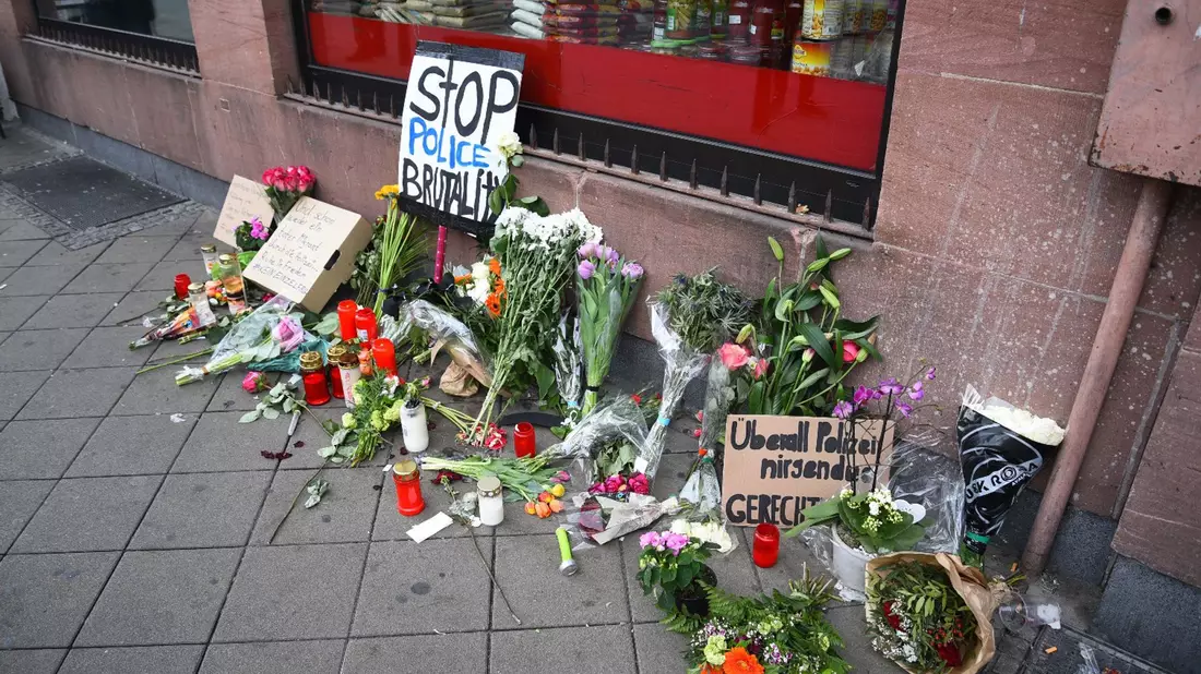 Blumen, Kerzen und Schilder liegen in Mannheim an dem Ort, an dem ein Mann Anfang Mai 2022 nach einer Polizeikontrolle starb. - Bild: René Priebe/PR-Video /dpa