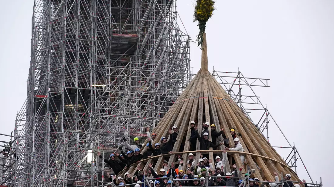Arbeiter feiern den Abschluss des Wiederaufbaus des Dachstuhls der Kathedrale Notre Dame mit einem traditionellen Blumenstrauß. - Bild: Christophe Ena/AP/dpa