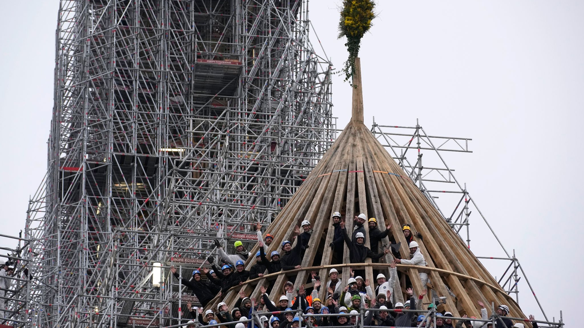 Arbeiter feiern den Abschluss des Wiederaufbaus des Dachstuhls der Kathedrale Notre Dame mit einem traditionellen Blumenstrauß. - Foto: Christophe Ena/AP/dpa