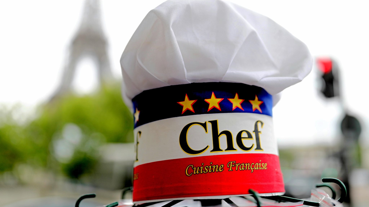 Eine Kochmütze wird an einem Souvenirstand beim Eiffelturm angeboten. In Frankreichs Gastronomie werden viele Stellen von Ausländern besetzt. - Foto: Michael Kappeler/dpa