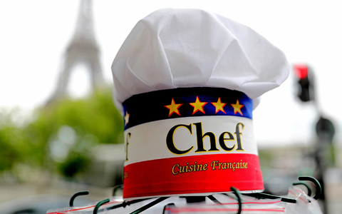 Eine Kochmütze wird an einem Souvenirstand beim Eiffelturm angeboten. In Frankreichs Gastronomie werden viele Stellen von Ausländern besetzt. - Foto: Michael Kappeler/dpa