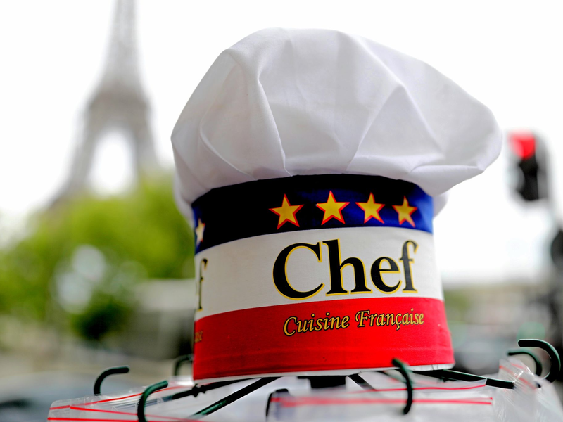 Eine Kochmütze wird an einem Souvenirstand beim Eiffelturm angeboten. In Frankreichs Gastronomie werden viele Stellen von Ausländern besetzt. - Foto: Michael Kappeler/dpa