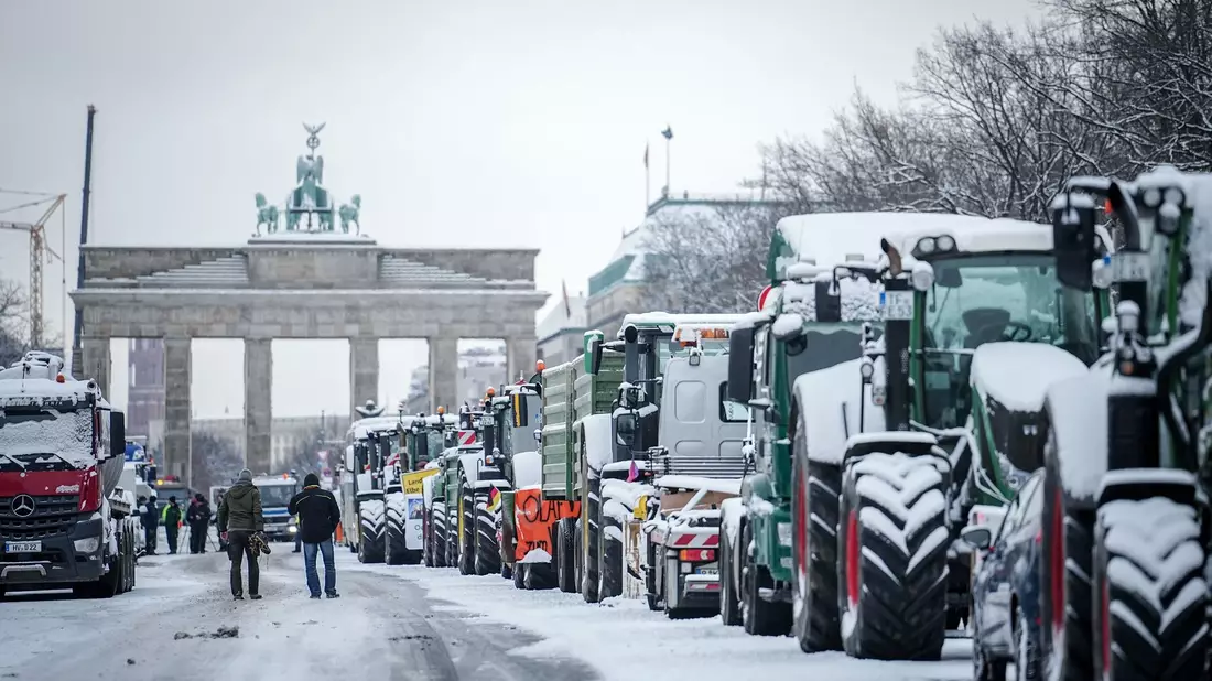 Zahlreiche schneebedeckte Traktoren stehen auf der Straße des 17. Juni vor dem Brandenburger Tor in Berlin. - Bild: Kay Nietfeld/dpa