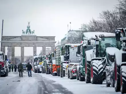 Zahlreiche schneebedeckte Traktoren stehen auf der Straße des 17. Juni vor dem Brandenburger Tor in Berlin. - Foto: Kay Nietfeld/dpa