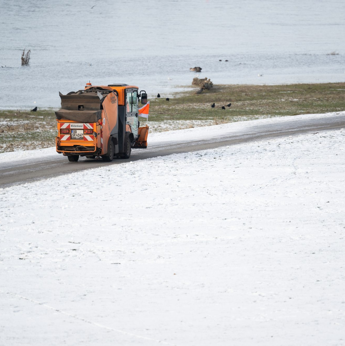 Ein Winterdienst-Fahrzeug fährt am Vormittag an den verschneiten Elbwiesen auf dem Radweg in Dresden entlang. - Foto: Robert Michael/dpa
