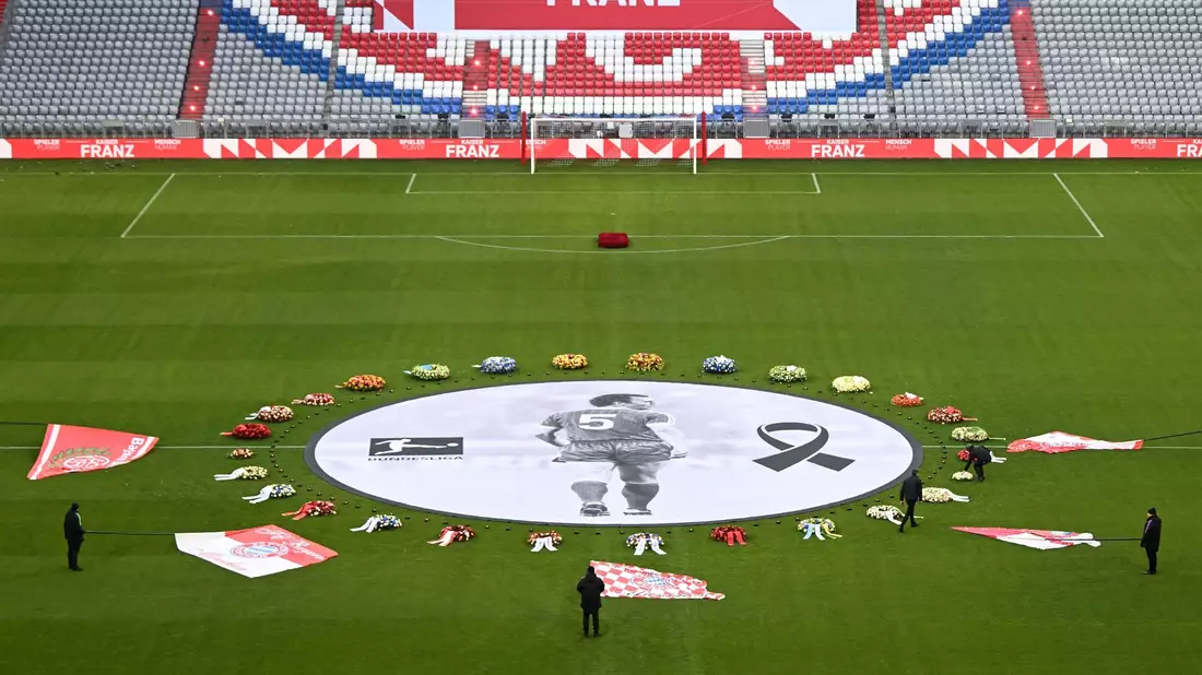 Fahnen von FCB-Fanclubs liegen neben einem überlebensgroßen Beckenbauer-Bild im Mittelkreis der Allianz Arena. - Bild: Sven Hoppe/dpa