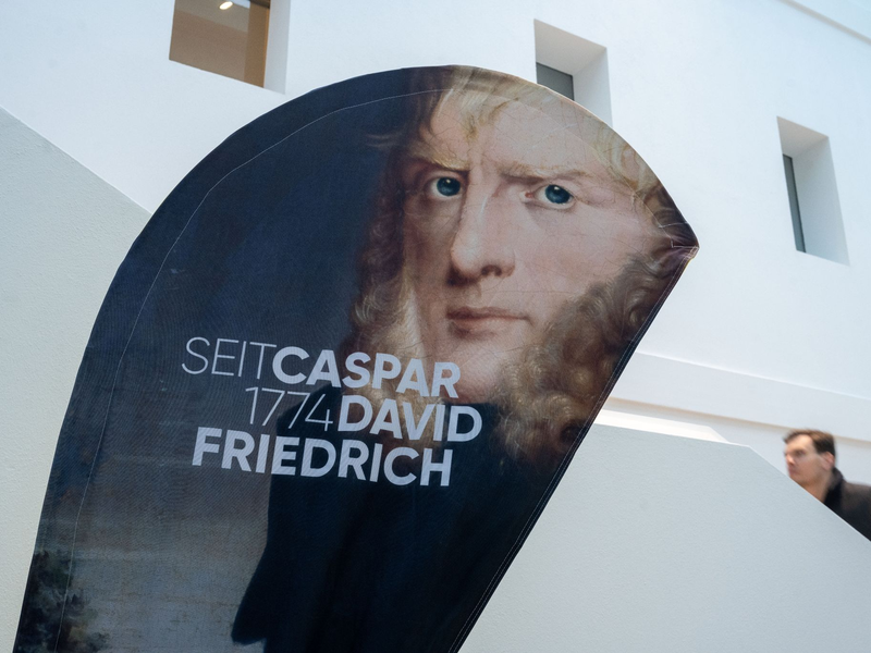 Ein Aufsteller mit einem Porträtbild von Caspar David Friedrich steht im Greifswalder Landesmuseum. - Foto: Stefan Sauer/dpa