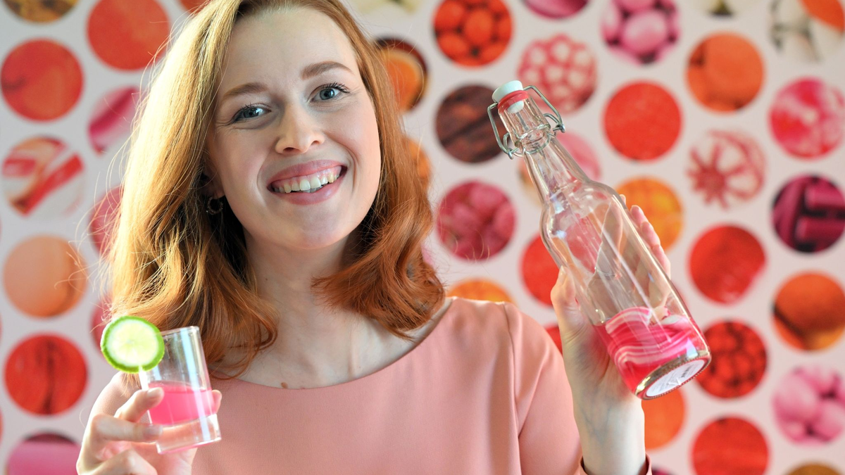 Model Christin hält auf der  Internationalen Süßwarenmesse ein Glas Wodka in der Hand, das mit Sweet Shots-Bonbonmasse versetzt wurde. - Foto: Federico Gambarini/dpa