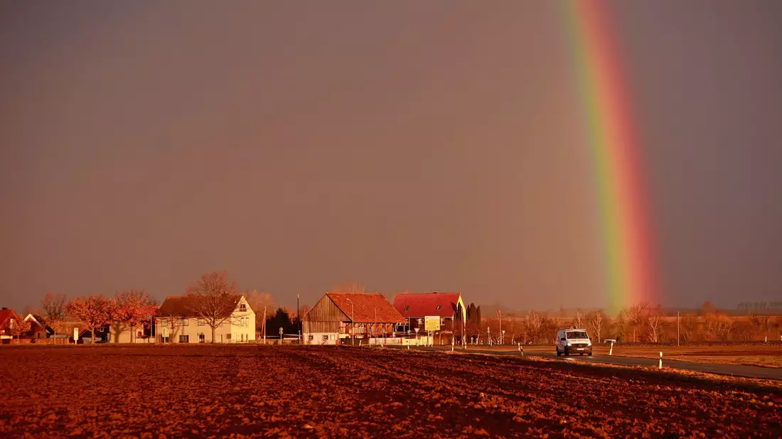 Ein Sturmtief kündigt sich bei tief stehender Sonne mit starkem Wind an, während sich ein Regenbogen am Himmel gebildet hat. - Bild: Matthias Bein/dpa