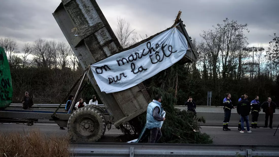 Landwirte kippen Zweige und Äste auf die Fahrbahn, während sie eine Autobahn in der Nähe von Lyon blockieren. - Bild: Laurent Cipriani/AP/dpa