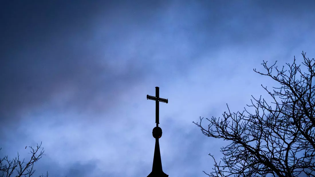 Dunkle Wolken über einem Kreuz einer Kirche: Einem der Missbrauchsopfer muss Schadenersatz gezahlt werden (Symbolbild). - Bild: Julian Stratenschulte/dpa