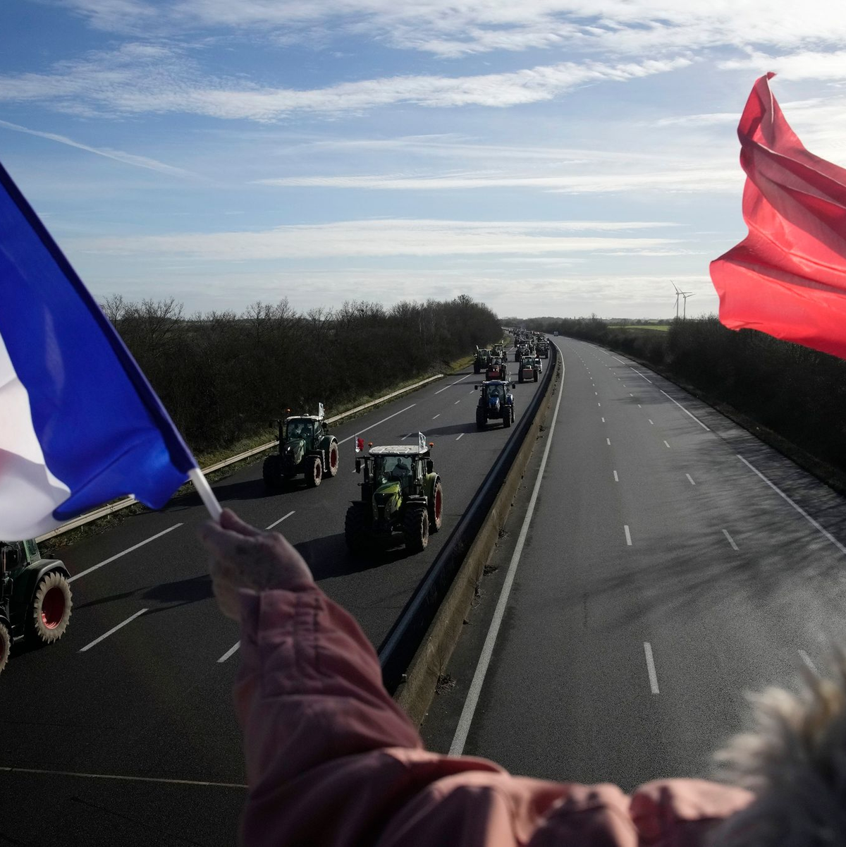 Eine Frau jubelt Landwirten mit französischen Fahnen zu. - Foto: Christophe Ena/AP/dpa