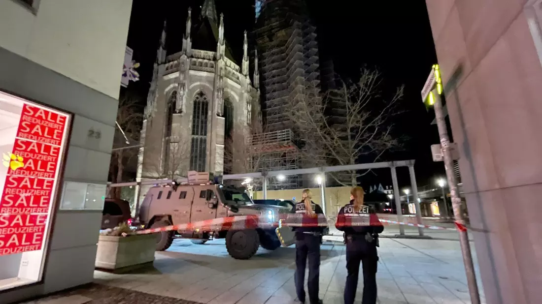 Zwei Polizistinnen stehen hinter einem Absperrband der Polizei am Münsterplatz. - Bild: Nico Pointner/dpa