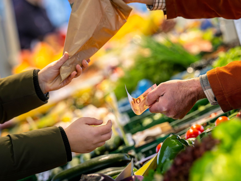 An einem Marktstand wird mit Bargeld eingekauft: Höhere Teuerungsraten schmälern die Kaufkraft von Verbrauchern. - Foto: Sina Schuldt/dpa