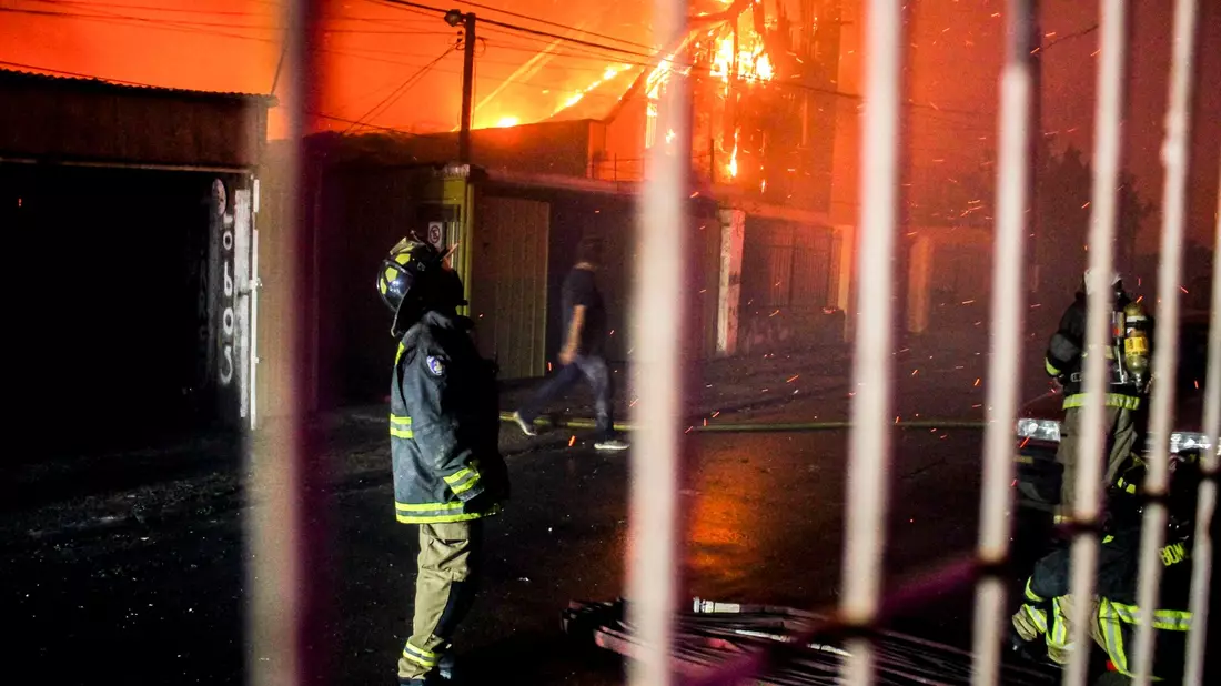 Ein Feuerwehrmann blickt nach oben, als die Flammen eines Waldbrandes auf Gebäude übergreifen. - Bild: Cristobal Basaure/AP