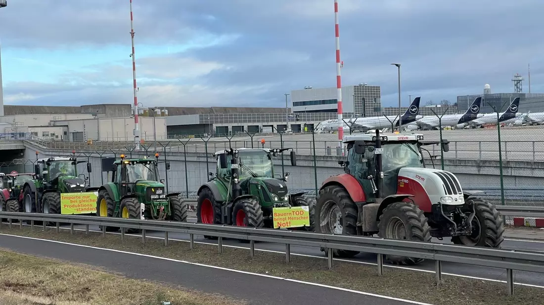 Traktoren fahren auf einer Straße am Flughafen Frankfurt vorbei. Wie ein Polizeisprecher sagte, begaben sich die Bauern am Morgen gegen 6 Uhr Richtung Airport. Geplant sei eine Protestfahrt rund um das Gelände. - Bild: Mike Seeboth/dpa