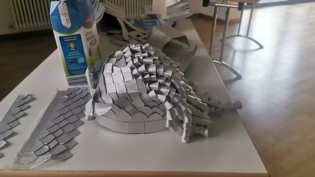 Ein kunstvoller Helm, der aus alten Milchtüten gebastelt wurde, liegt auf einem Tisch. - Bild: Ramona Wahner/Deutsche Fastnachtakademie/dpa
