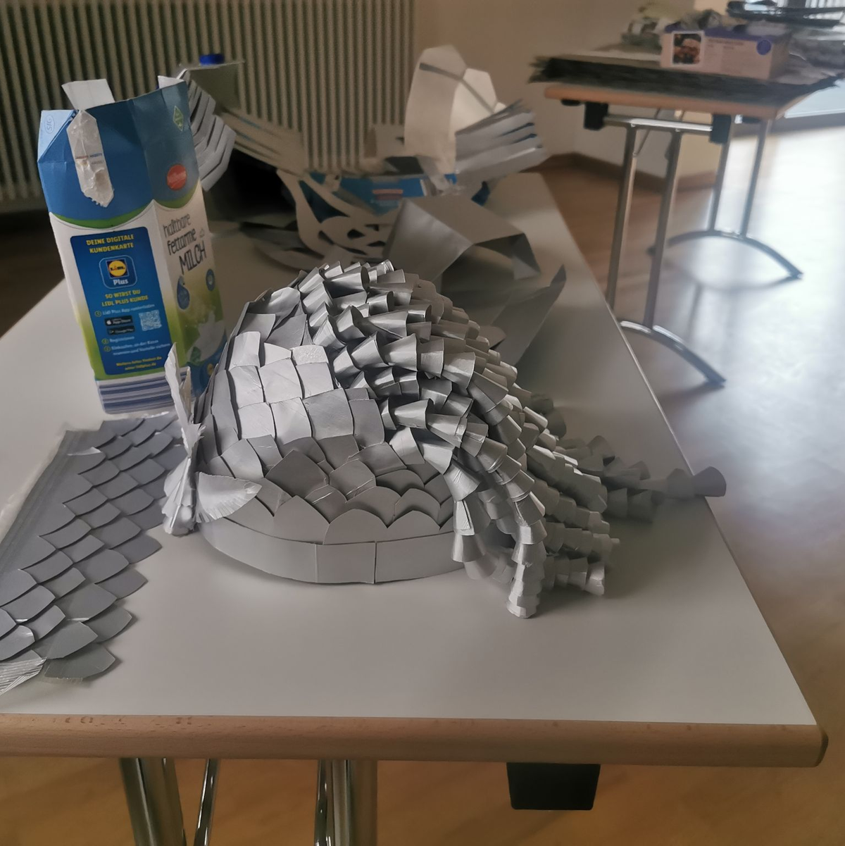 Ein kunstvoller Helm, der aus alten Milchtüten gebastelt wurde, liegt auf einem Tisch. - Foto: Ramona Wahner/Deutsche Fastnachtakademie/dpa