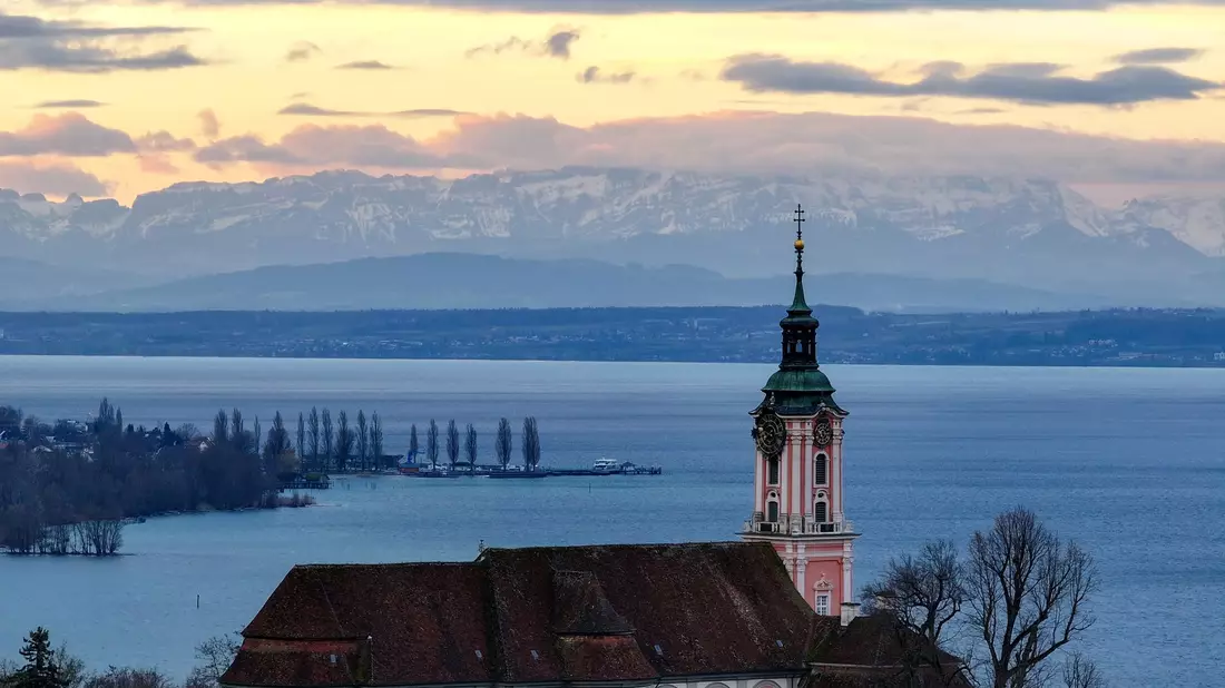 Hinter der ehemaligen Klosterkirche Birnau am Bodensee geht die Sonne auf. Die Alpen sind im Hintergrund zu sehen. - Bild: Felix Kästle/dpa