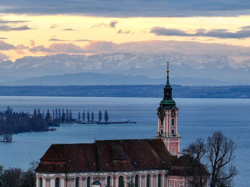 Hinter der ehemaligen Klosterkirche Birnau am Bodensee geht die Sonne auf. Die Alpen sind im Hintergrund zu sehen. - Foto: Felix Kästle/dpa