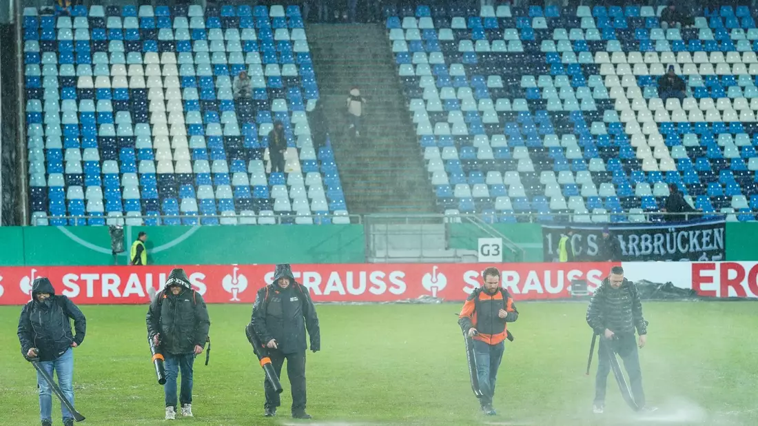 Im Ludwigspark-Stadion versuchen Helfer, Wasserlachen vom Spielfeld zu entfernen. - Bild: Uwe Anspach/dpa