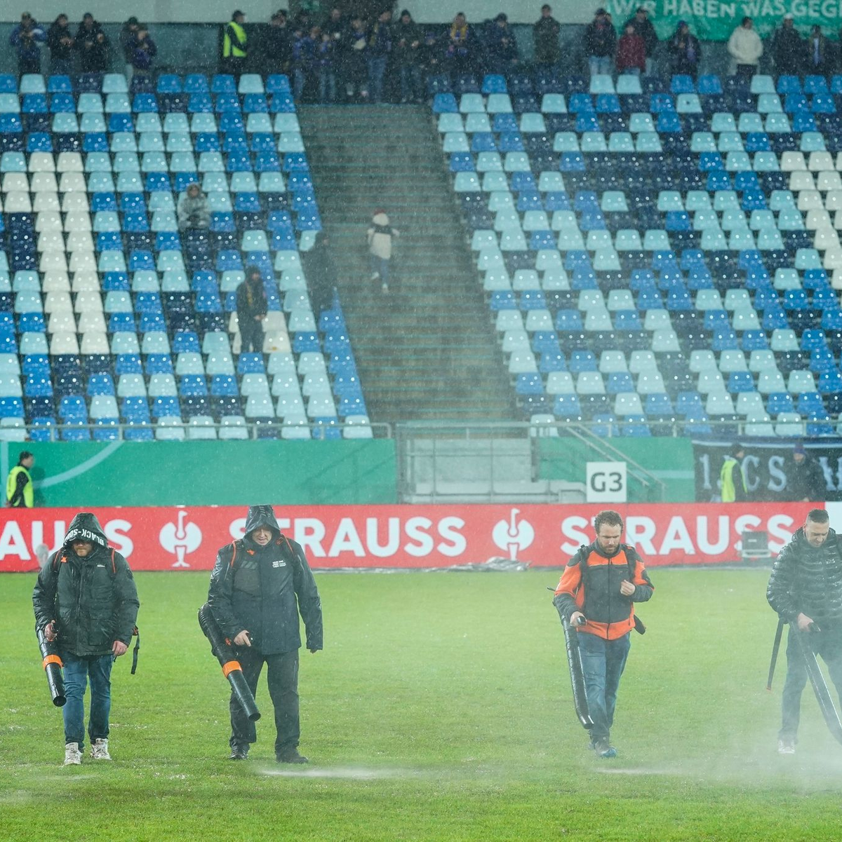 Im Ludwigspark-Stadion versuchen Helfer, Wasserlachen vom Spielfeld zu entfernen. - Foto: Uwe Anspach/dpa
