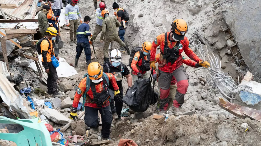 Rettungskräfte tragen ein Opfer aus dem von einem Erdrutsch betroffenen Dorf Masara. - Bild: Uncredited/AP/dpa
