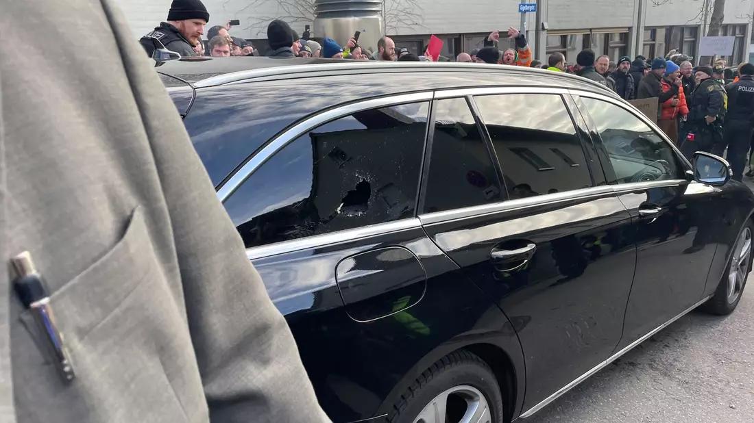 Ein Auto mit eingeschlagener Scheibe vor der Veranstaltungshalle. - Bild: David Nau/dpa