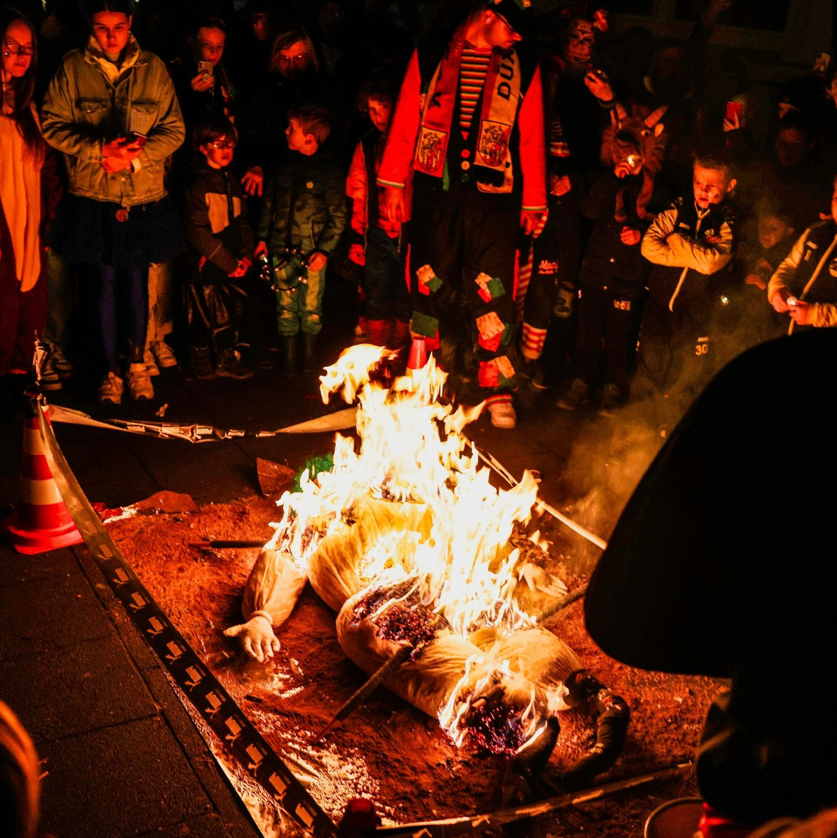 Karnevalisten verfolgen die Verbrennung des Nubbels in Köln. - Foto: Oliver Berg/dpa