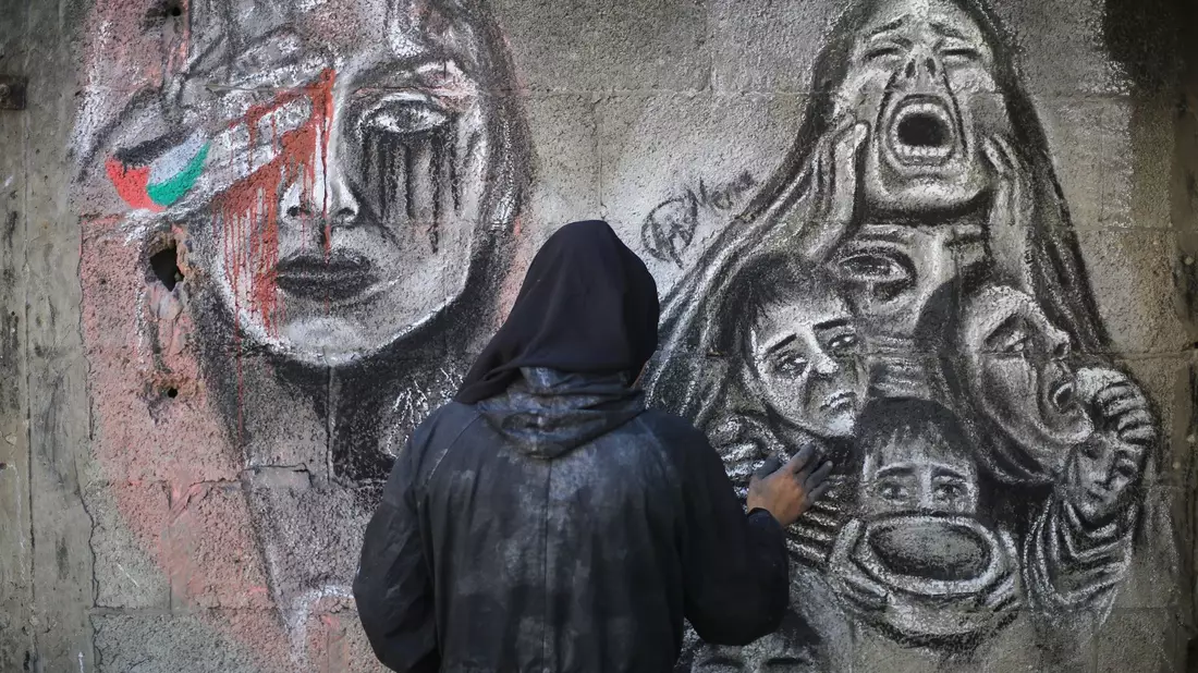 Eine palästinensische Künstlerin bemalt mit Kohle die Wände einer Schule in Deir al-Balah im Zentrum des Gazastreifens, in die sie umgesiedelt wurde. - Bild: Mohammed Talatene/dpa
