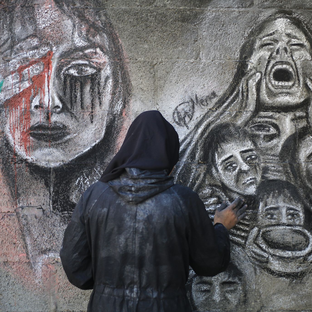 Eine palästinensische Künstlerin bemalt mit Kohle die Wände einer Schule in Deir al-Balah im Zentrum des Gazastreifens, in die sie umgesiedelt wurde. - Foto: Mohammed Talatene/dpa