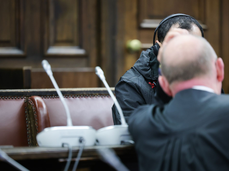 Einer der beiden Angeklagten (verdeckt) spricht mit seinem Anwalt Hannes Linke vor Prozessbeginn im Gerichtssaal des Strafjustizgebäudes. - Foto: Christian Charisius/dpa-Pool/dpa