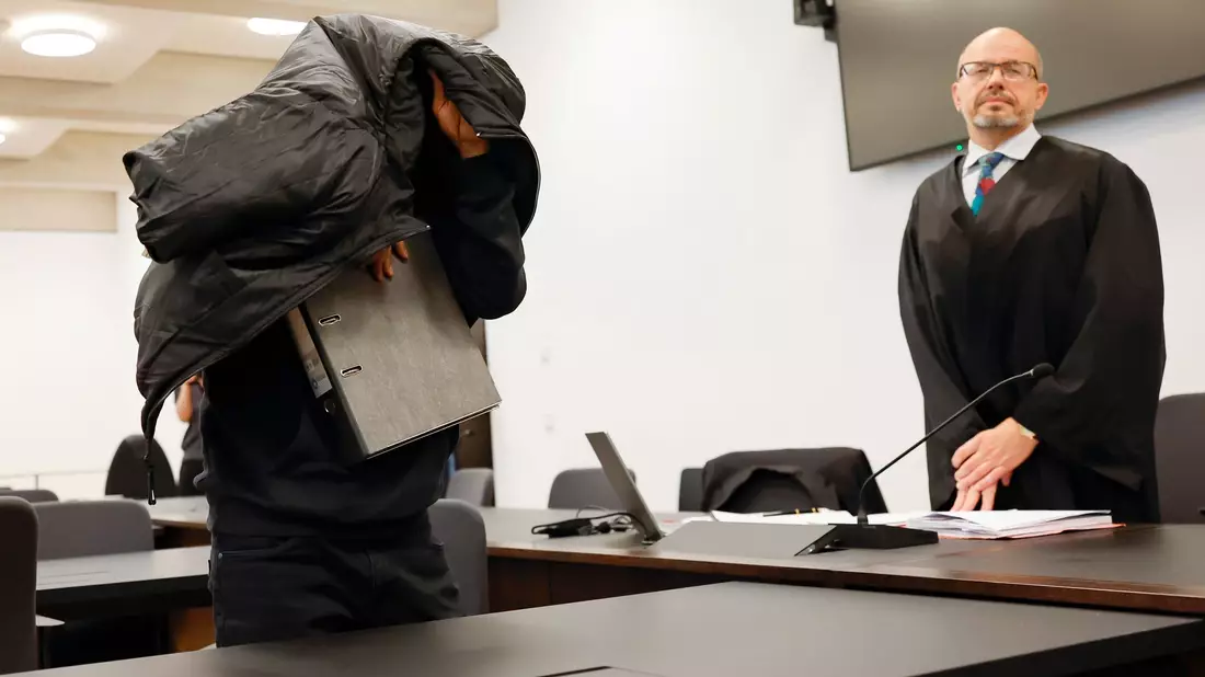 Der ehemalige Security-Mann bedeckt im Gerichtsaal seinen Kopf mit einer Jacke. - Bild: Daniel Löb/dpa