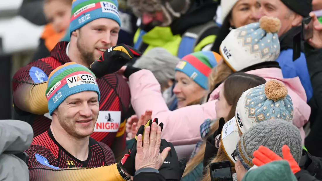Francesco Friedrich (vorne l) und Alexander Schüller (hinten l) klatschen nach ihrem Sieg mit Fans ab. - Bild: Robert Michael/dpa
