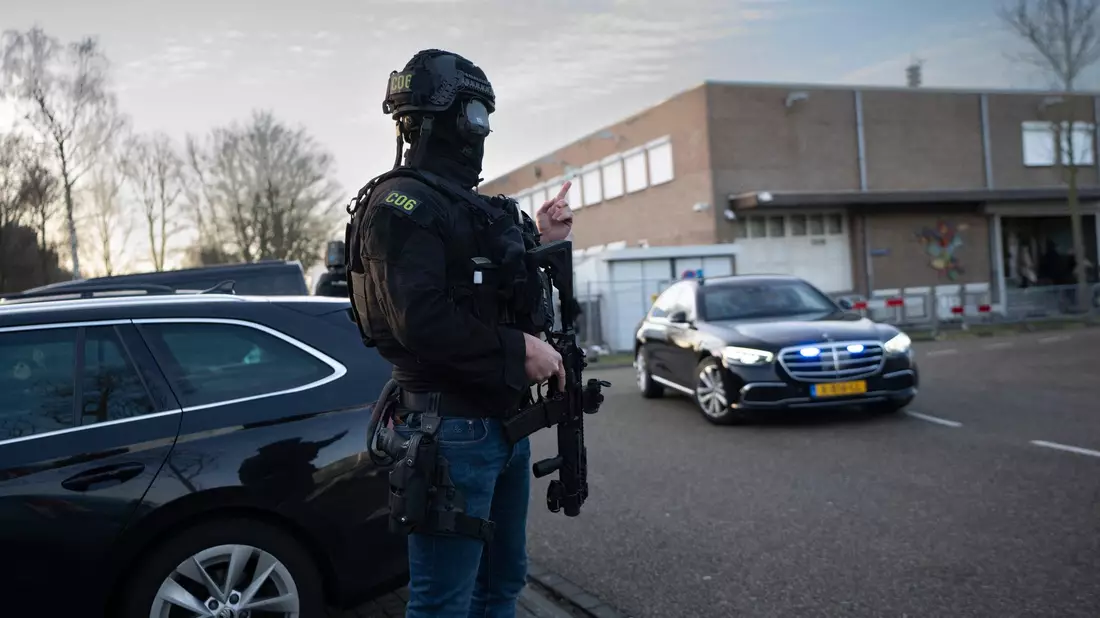 Maskierte und bewaffnete niederländische Polizisten bewachen einen Transport mit einigen der Verdächtigen, die vor dem Hochsicherheitsgebäude des Gerichts in Amsterdam eintreffen. - Bild: Peter Dejong/AP/dpa